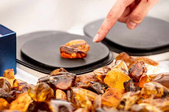 Various pieces of amber on a table with a hand weighing a piece on a scale in the background