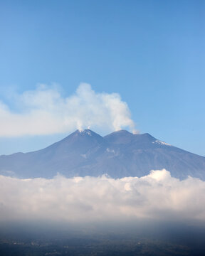 Mount Etna volcano smoking above clouds seen from Taormina in Sicily, Italy.