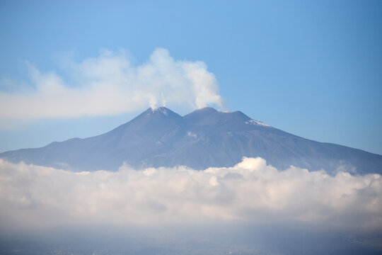 Mount Etna volcano smoking above clouds seen from Taormina in Sicily, Italy.