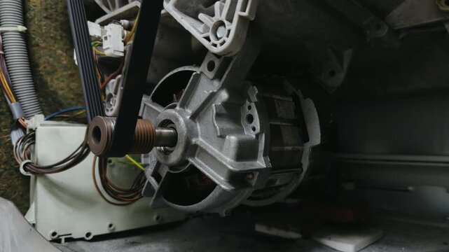 Close up of an electric motor and drive belt spinning on a washing machine during appliance repair and maintenance service.	
