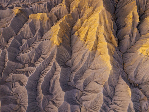 Aerial view of Caineville Mesa featuring eroded badlands with intricate drainage patterns highlighted by golden sunlight and deep shadows in Wayne County, Utah, United States.