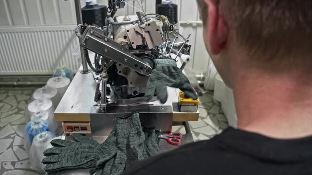 Mechanical head of an automated overedging device trims and binds the elastic cuff of a fabric glove on modern factory line.