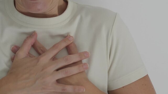 A woman wearing a white shirt suddenly bringing both hands to her chest while reacting with a startled scream. The expressive body gesture represents fright, shock, surprise or an unexpected emotion