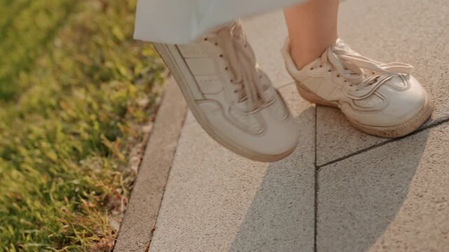 Woman feet in white sneakers move along sunlit stone pavement capturing rhythmic motion of walking. focus remains on her lower legs and shoes as they shift from one tile to another with soft