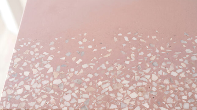 Blush pink terrazzo surface with scattered white and grey stone chips, close-up texture background