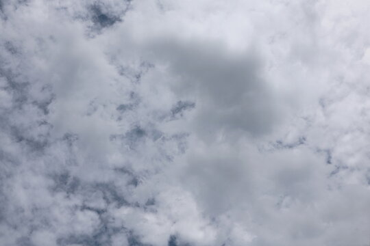 The sky is covered with thick clusters of gray and white clouds. The clouds are a mix of gray and white tones. These are altocumulus vs stratocumulus clouds. Signs before a storm
