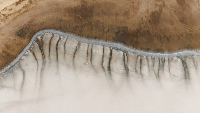 Aerial view of the salt lake landscape near Ballidu, featuring intricate erosion patterns and contrasting textures of brown earth and white salt crust in Ballidu, Western Australia, Australia.