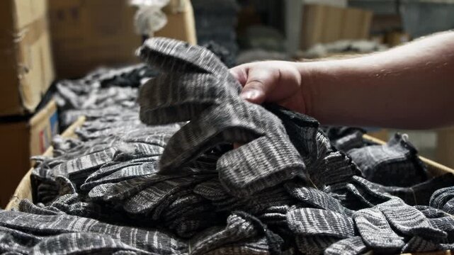 Close up of worker inspecting finished knitted construction gloves during quality control process. Hand checks material, stitching and overall condition before packaging.