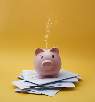Pink Piggy Bank Smoking on Top of Envelopes Representing Burning Savings