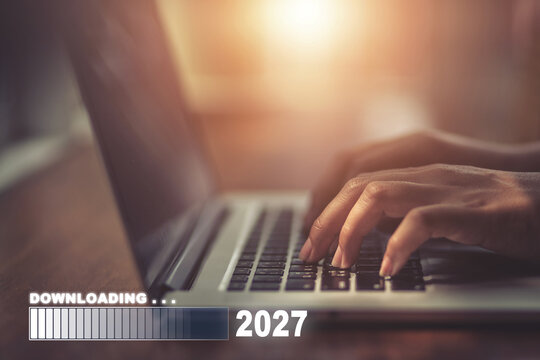 Hands typing on laptop keyboard with downloading progress bar showing 2027, remote work and technology concept