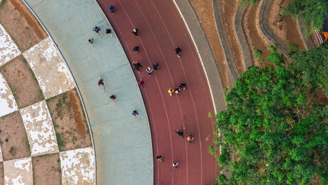 Aerial view of people running on a red athletic track with a light blue lane and lush green trees in Indonesia.