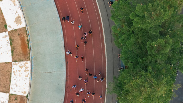 Aerial view of runners on a red athletic track with green trees and a checkered pattern on the side in Indonesia.