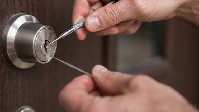 Hands manipulating lock picks on a metallic door lock cylinder