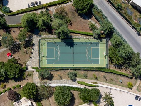 Aerial view of a green tennis court surrounded by lush trees and stone pathways in a park setting in Sariyer, Istanbul, Turkey.