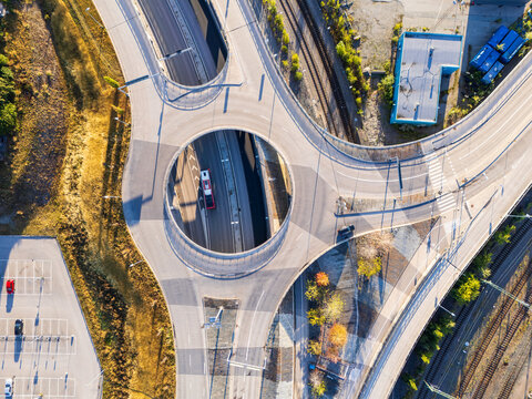 Aerial view of the E20 highway roundabout near Vartahamnen with surrounding railway tracks, a parking lot, and urban infrastructure in Stockholm, Stockholm County, Sweden.