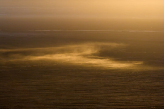 Aerial view of Atacama desert with golden light illuminating blowing sand and dust across the vast arid landscape in Chile.