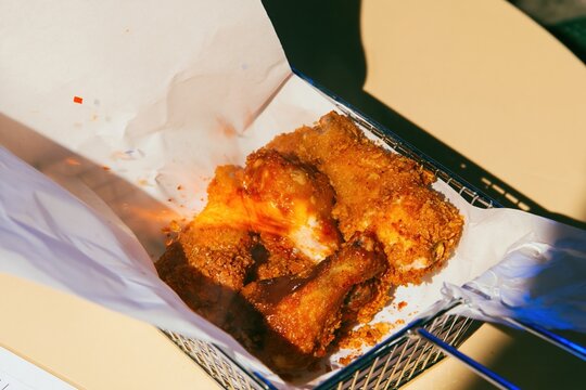 Breaded chicken drumsticks in a wire basket with crumpled paper on a stone tabletop, featuring crunchy textures for takeout and comfort food campaigns
