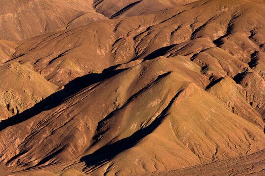 Aerial view of the rugged and arid mountain slopes of the Atacama desert, featuring deep shadows and textured terrain in Chile.