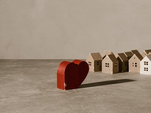 Red heart shaped house model standing out among rows of tan miniature homes on a grey surface, for home search and rental selection