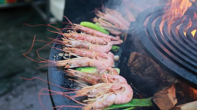 Fresh shrimp grilling on round charcoal barbecue with flames and smoke. Seafood cooking on grill with zucchini at street food stall. Delicious prawns preparation closeup