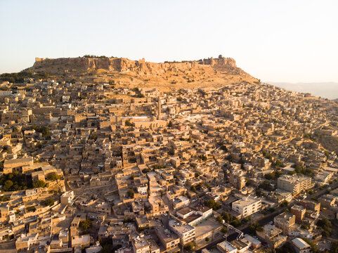 Aerial view of the historic city of Mardin with its traditional stone houses and the ancient castle perched on the hill under warm golden hour light in Mardin, Mardin, Turkey
