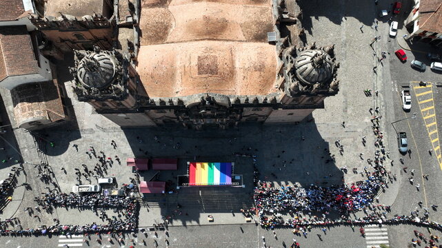 Aerial view of Cusco Cathedral and the Plaza de Armas with a rainbow flag on a stage and crowds of people gathered on the stone square in Cusco, Cusco, Peru.