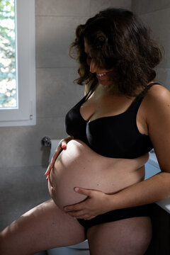 Pregnant woman feeling her baby bump in the bathroom, anticipating motherhood