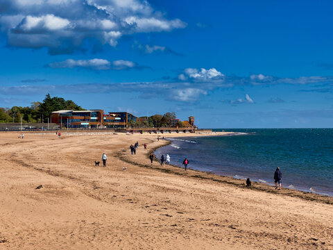 Sunny day at the coastal beach with sandy shore, promenade, and blue sky with white clouds