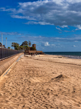 Sunny day at the coastal beach with sandy shore, promenade, and blue sky with white clouds