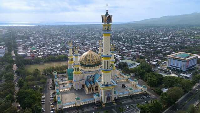 Aerial view of Hubbul Wathan Mosque with its prominent golden dome and tall minarets, surrounded by the urban landscape of Mataram in Indonesia.