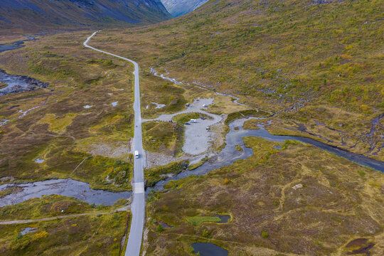 Aerial view of Slettvikane featuring a road crossing a bridge over a winding stream, surrounded by tundra landscape and a small parking area with a camper van in Fjord, More og Romsdal, Norway.