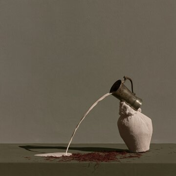 Stream of milk flowing upward from a brass tumbler into a muslin vessel on a dark ledge, with a clean wall for copy space and dairy branding