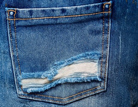 close up image of a ripped back denim pocket on a blue jean texture background with space for copy