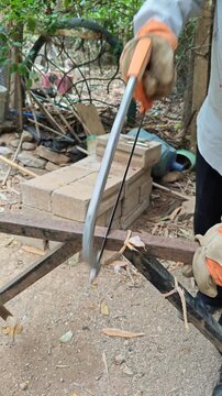 Hand in work glove using a hacksaw to cut through metal pipe