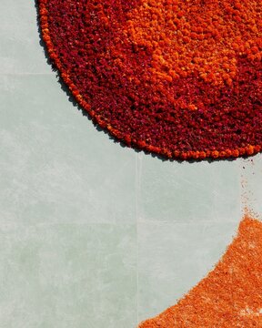 Colorful floral mandala made of marigold petals on a pale grey-green stone floor with copy space for cultural festivals and crafts