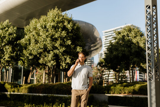 Man talking on phone at modern urban park with greenery and buildings