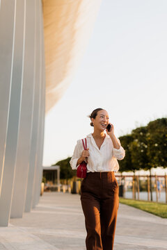 Confident Korean woman strolling and chatting on the phone during golden hour