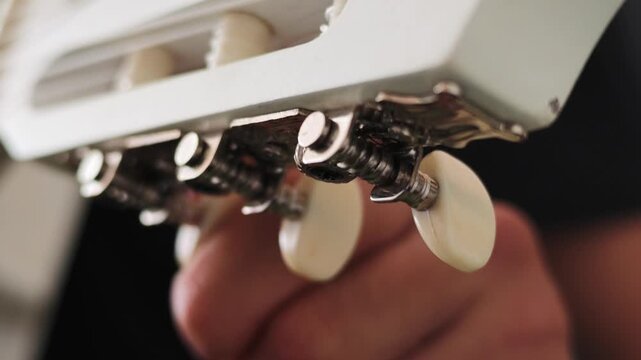A hand adjusts the tuning pegs on a white guitar headstock, rotating the cream-colored knobs with precise, deliberate motions to fine-tune the strings.