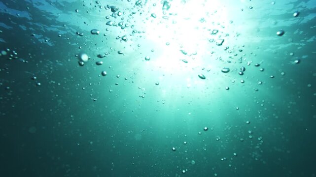 Air bubbles rise toward bright sunlight through clear turquoise ocean water underwater