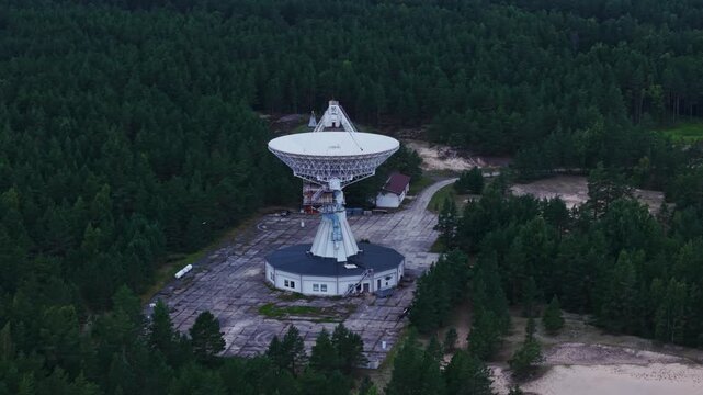 White astronomy dish towers above dark pine woodland in Irbene, Latvia