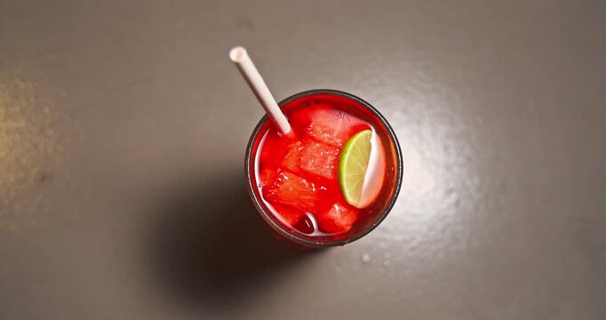Top view of fresh cold watermelon cocktail with lime slice and paper straw on modern restaurant table. Refreshing summer iced fruit drink at tropical resort. Hotel vacations concept.