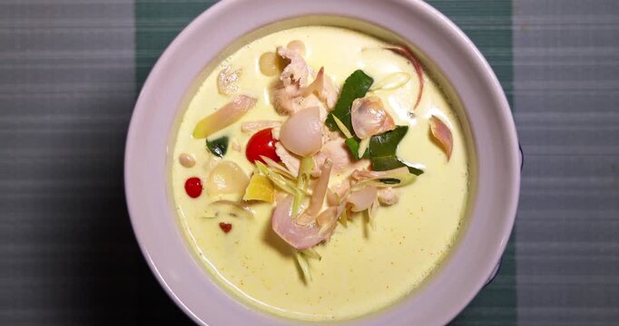 Traditional Thai Tom Kha Gai coconut chicken soup with galangal and herbs in ceramic bowl on table. Delicious authentic spicy Asian cuisine at holiday resort. Thai food travel concept.