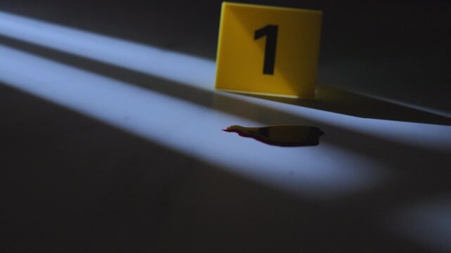 Blood puddle beside yellow evidence marker on floor with window shadow for forensic crime scene concept, slow zoom in close up shot⁠