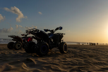 All-terrain vehicles ATV parked on sandy beach during golden hour sunset © panji