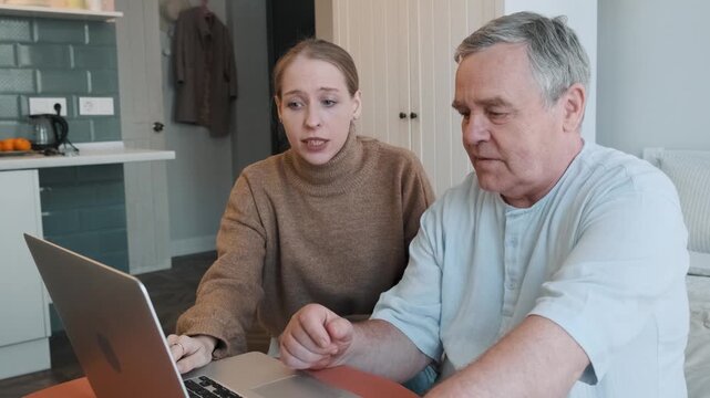 Young adult daughter teaches her senior father how to use laptop at home. Technology education, computer training, digital literacy, lifelong learning, generation gap, family assistance