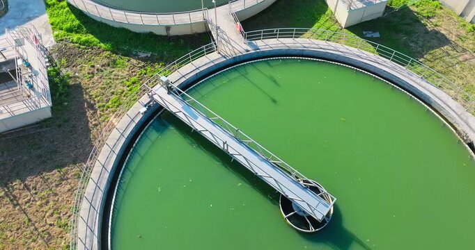 Aerial view of circular water basins with green and blue water, metal walkways, railings, concrete structures, and bright sunlight.