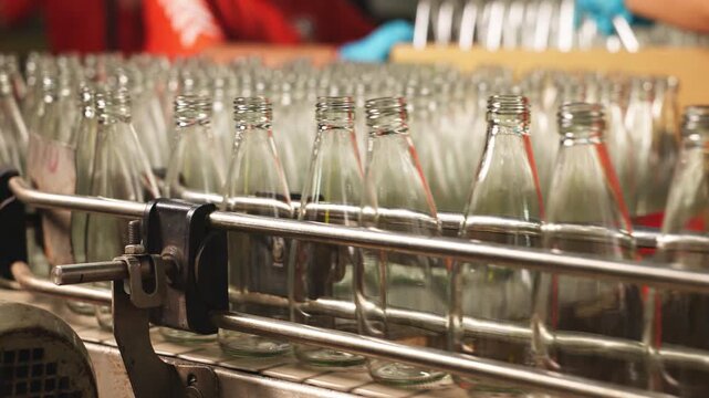 Close-up of industrial bottling equipment precisely filling glass containers with liquid during high-speed beverage production process in factory