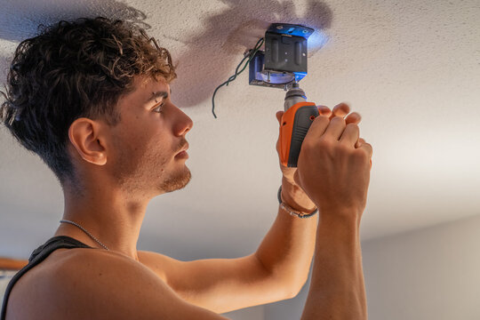 Young person installing a ceiling lamp with an electric screwdriver during a home repair