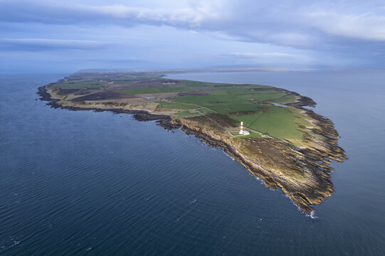 Tain, Scotland, United Kingdom - 10 April 2024: Aerial view of Tarbat Ness Lighthouse situated on a rocky peninsula surrounded by green fields and the North Sea.
