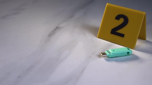 USB drive next to yellow evidence marker 2 on white marble surface for digital forensics cyber crime investigation with copy space, handheld 45 degree angle shot